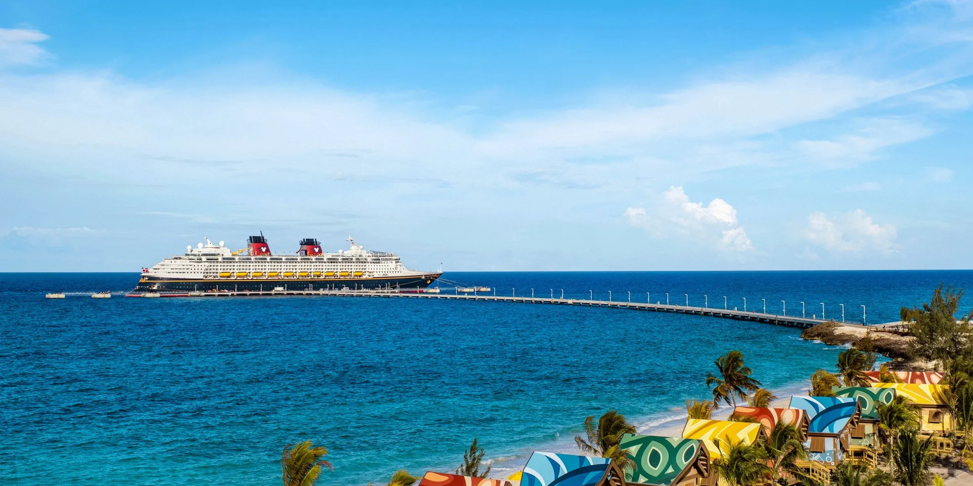 A Disney Cruise Ship docked off of the shore of a tropical island.