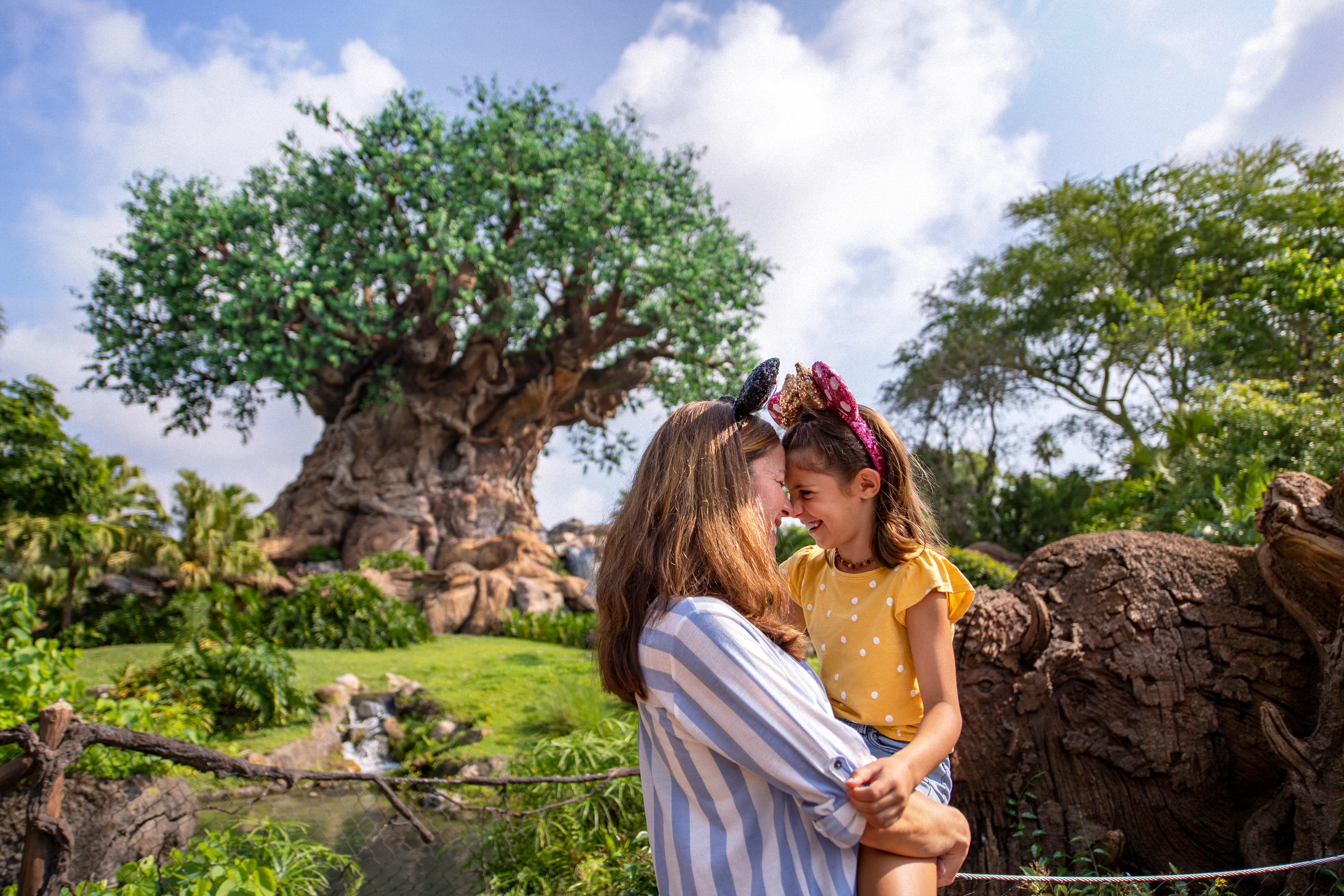A mother and daughter wearing Mickey Mouse ears share a loving moment in front of the Tree of Life at Disney's Animal Kingdom.