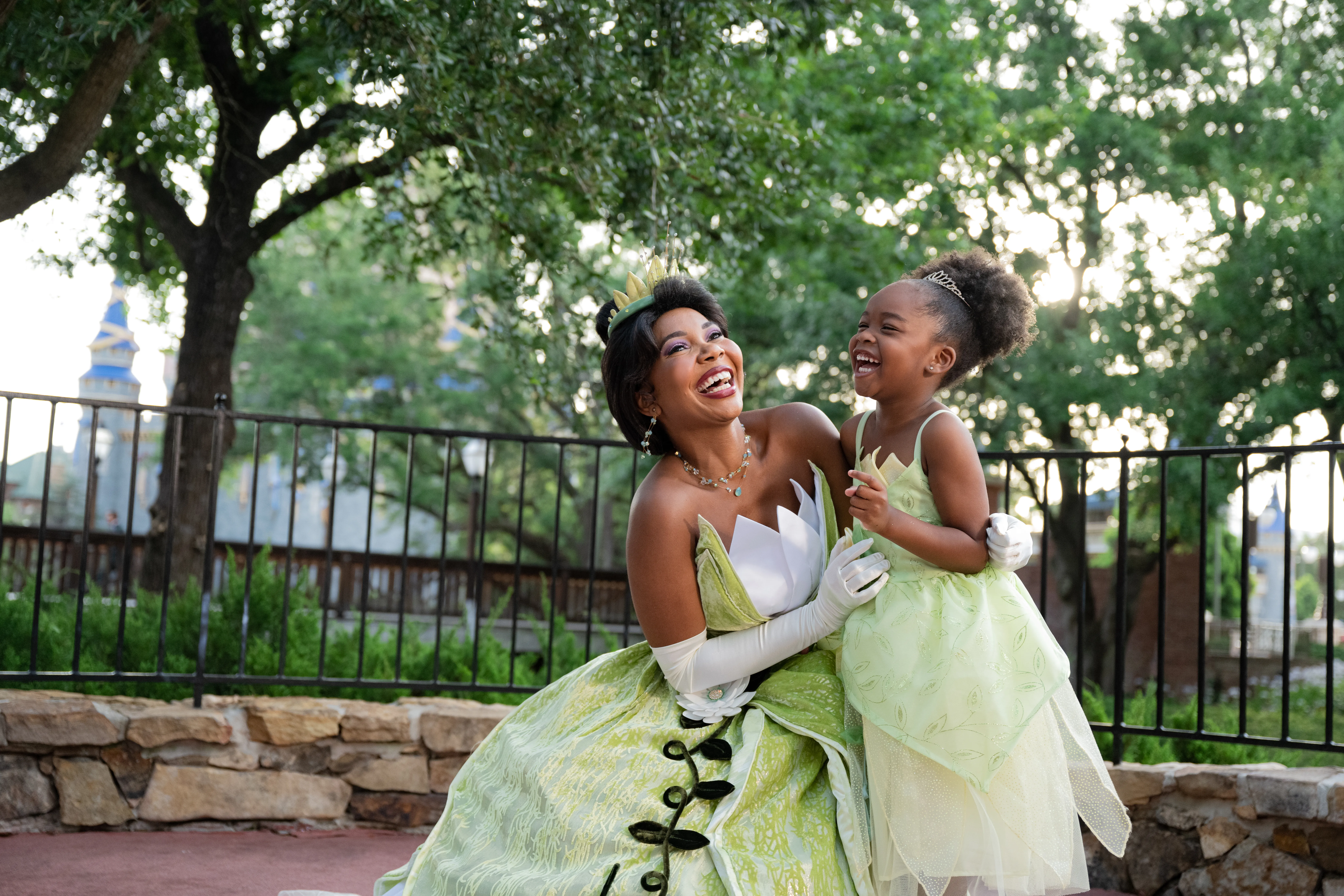Princess Tiana actress sharing a special moment with a young girl; the Magic Kingdom Castle can be seen in the background.